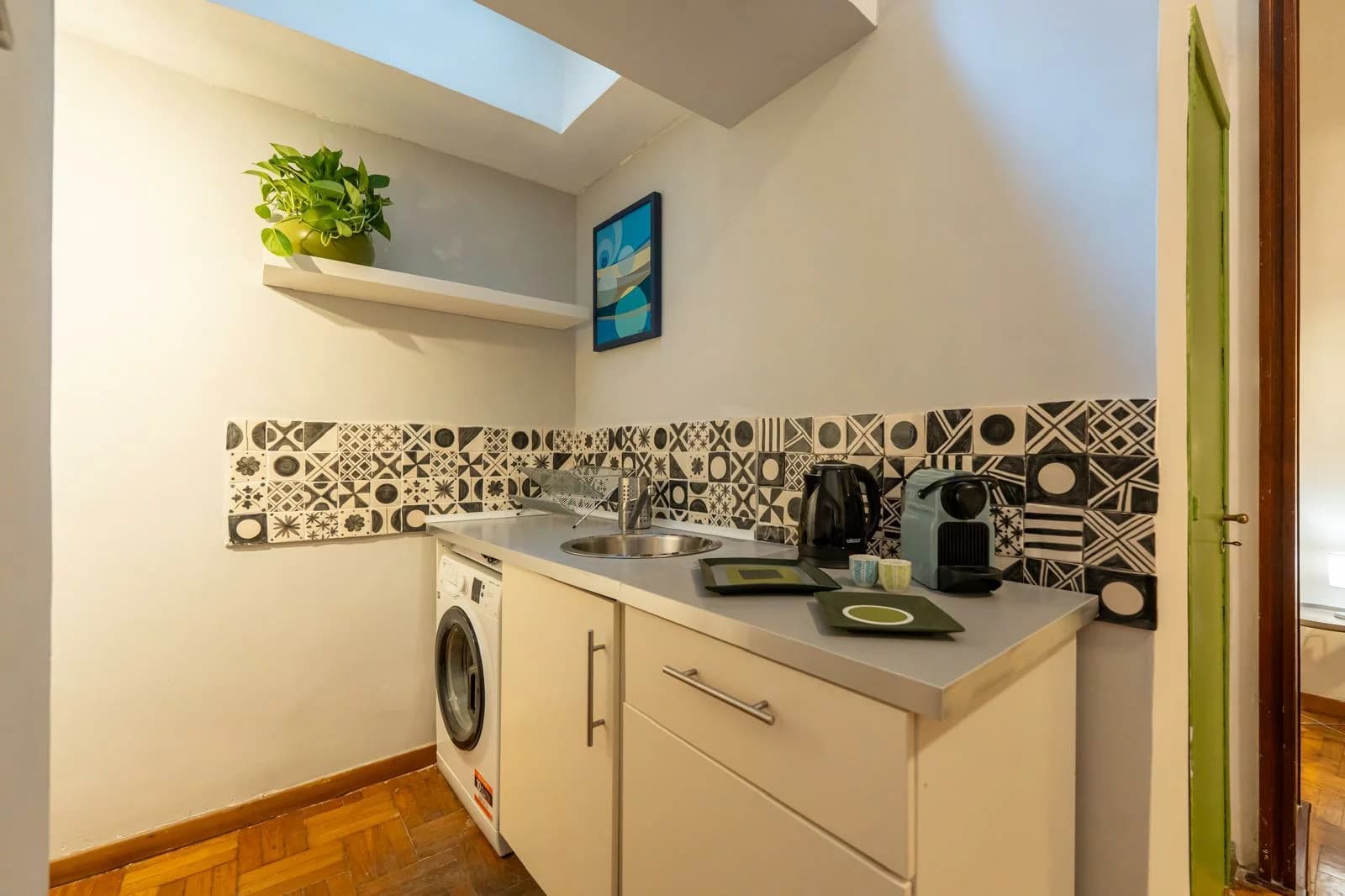 Cucina con piastrelle decorate, lavandino e lavatrice sotto il lucernario